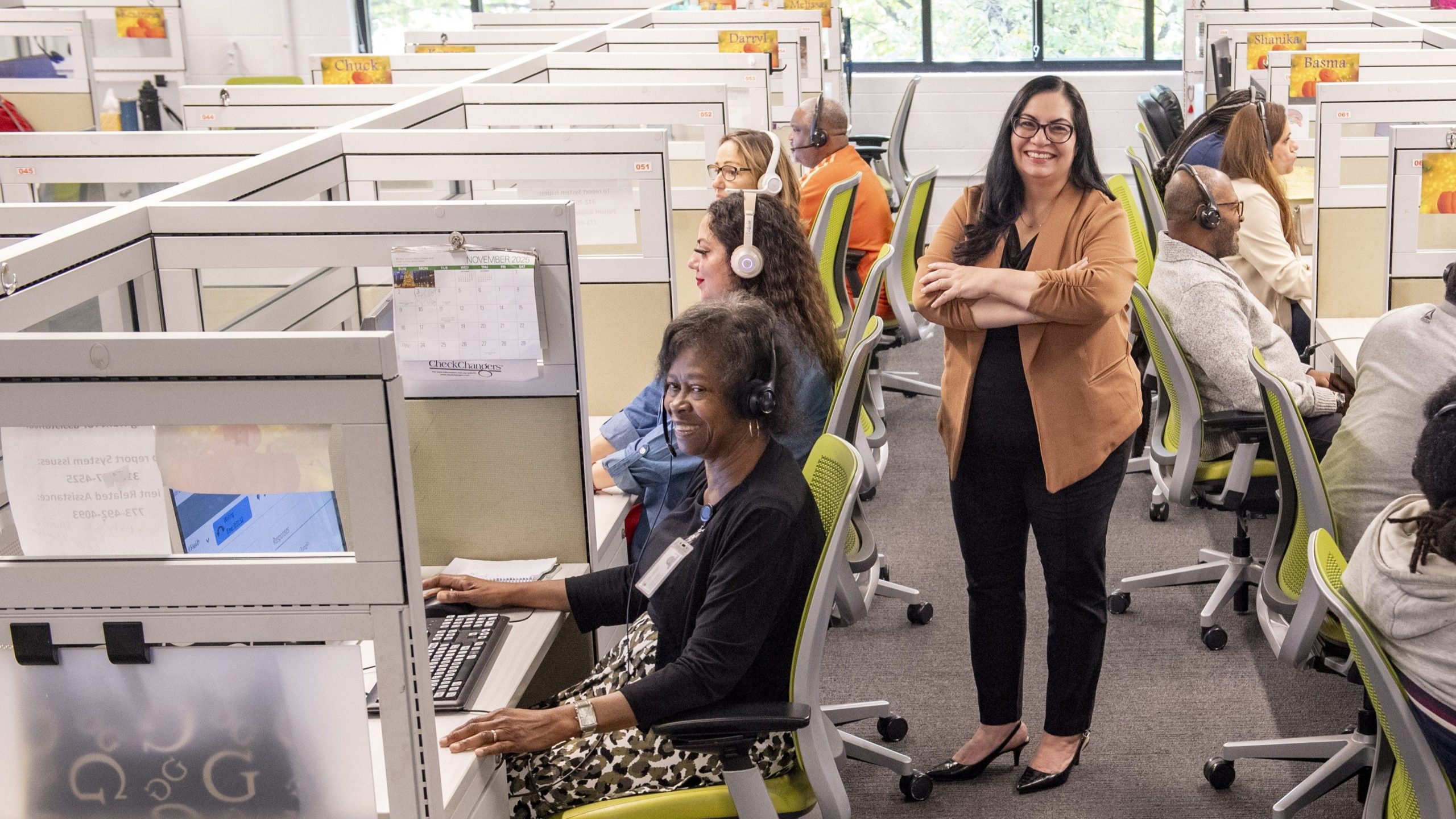 A Lighthouse Enterprises supervisor stands on the contact center floor beside agents working at their cubicles.