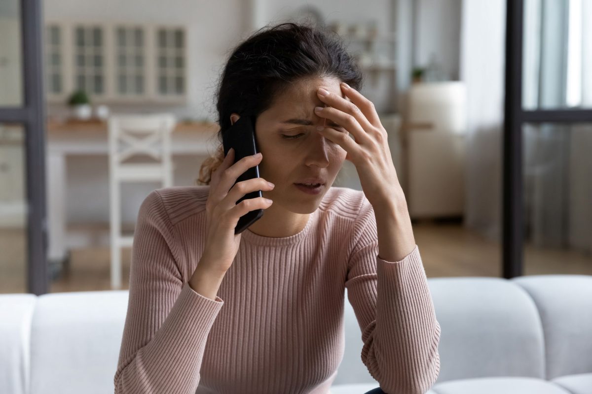 A woman talking on the phone. She is holding her hand to her forehead and looks stressed.