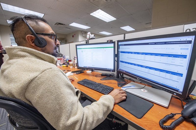 Support agent wearing a headset at a dual-monitor workstation in an open-office cubicle.