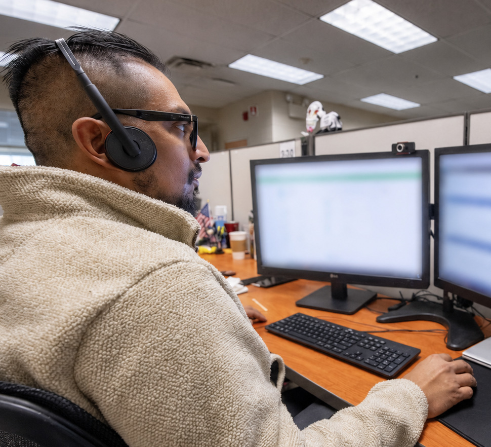 A Lighthouse Enterprises contact center agent wearing a headset works a customer support queue on dual monitors.